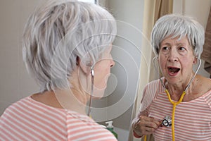 Comedic senior woman using an stethoscope on herself