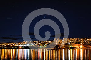 Comet Neowise over Rijeka port city on Adriatic sea, Croatia. Amazing night cityscape with city lights and blue starry sky