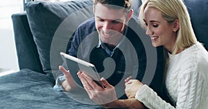 Comfort and connectivity combined. 4K video footage of a loving young couple using a digital tablet together on the sofa