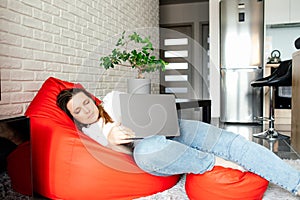 Comfort and work. Freelancer woman is comfortably sitting in bag chair and stretching her legs, working at laptop .