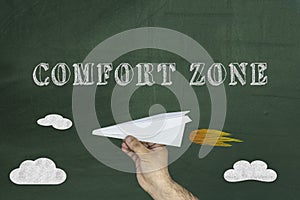 Comfort Zone Concept, Human hand holding paper airplane on chalkboard