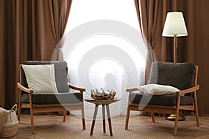 Comfortable armchairs near window with stylish curtains in living room. Interior design