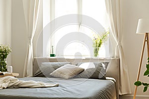 A comfortable bed with graphite bedding and cushions against a bright window in an eco friendly bedroom interior in a tenement hou