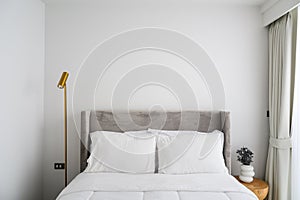 Comfortable bed in modern bedroom, pillows and white soft blanket on bed, lamp and vase decorate in room. Free white wall space