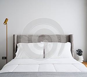 Comfortable bed in modern bedroom, pillows and white soft blanket on bed, lamp and vase decorate in room. Free white wall space