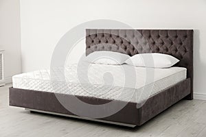 Comfortable bed with new mattress near wall in room.