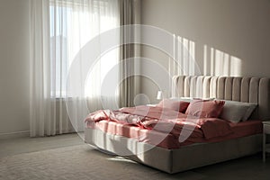 Comfortable bed with pink linens near beige wall