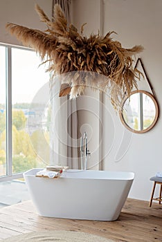 Comfortable bright bathroom with a boho-chic interior design, a free-standing white bath against the background of a panoramic