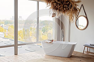 Comfortable bright bathroom with a boho-chic interior design, a free-standing white bath against the background of a panoramic