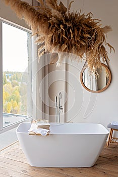 Comfortable bright bathroom with a boho-chic interior design, a free-standing white bath against the background of a panoramic