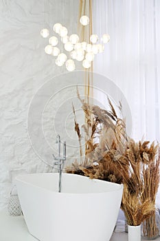 Comfortable bright bathroom with a boho-chic interior design, a free-standing white bath against the background of white