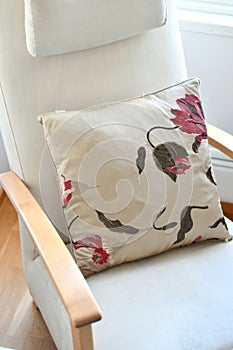 Comfortable chair with armrests and cushion. Beige pillow with pink flower pattern is elegant with neutral furniture