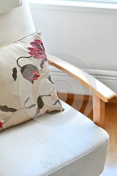 Comfortable chair with armrests and cushion. Beige pillow with pink flower pattern is elegant with neutral furniture