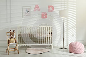 Comfortable crib near wall with pink letters in baby room. Interior design