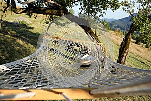Comfortable net hammock with hat and book in mountains on sunny day