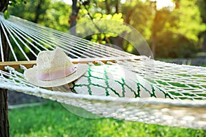 Comfortable net hammock with pillow and hat hanging in garden