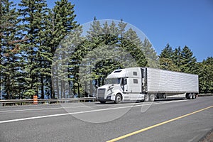 Comfortable pro white big rig semi truck transporting cargo in reefer semi trailer driving on the multiline highway road