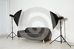 Comfortable sofa and professional lighting equipment in photo studio