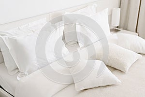Comfortable soft pillows on the bed. Close-up white bedding sheets and pillow on light wall room background. Fresh bed photo