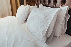 Comfortable soft pillows on the bed. Close-up white bedding sheets and pillow on light wall room background. Fresh bed concept