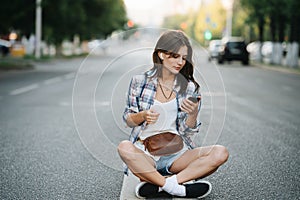 Comfortable woman sitting in the middle of an empty city road, phone in hand