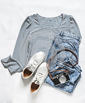 Comfortable women`s clothing for walking - a knitted T-shirt with long sleeves, jeans, sneakers and a camera on a light backgroun