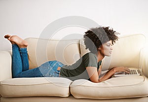 Comfortable and working. a young woman relaxing at home on the weekend while working on her laptop.