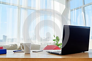 Comfortable workplace with  laptop computer, supplies and cup of coffee, copy space. Wood table in sunny office with big windows.