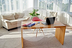 Comfortable workplace with  laptop computer, supplies and papers, copy space. Wood table in sunny office with big windows.