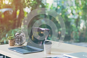 Comfortable workplace, Office desk with blank screen laptop and clock, plant, Nature light bokeh background.