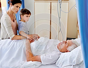 Comforting company for granddad. a sick man in a hospital bed being comforted by his daughter and grandson.