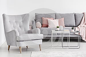 Comfy armchair and grey sofa with pink pillows, and coffee table photo