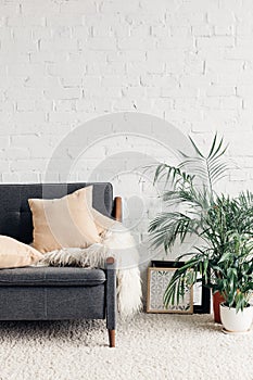 Comfy couch with flowerpots in white living room interior with brick wall