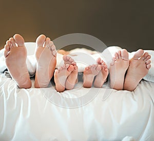 Comfy family lying in a bed together relaxing taking a nap together. Feet and toes of parents and their children being