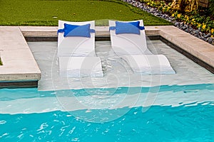 Comfy white loungers in shallow end of refreshing blue swimming pool in yard with flower trim around the edge photo