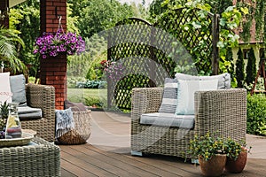 Comfy wicker armchair with pillows on wooden terrace of trendy suburban home