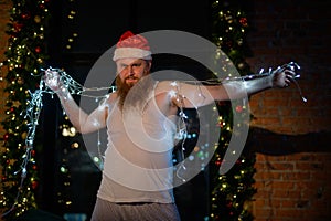 A comic image of santa claus in underwear on christmas eve. A man in a suit of Santa Claus holds a garland with lights