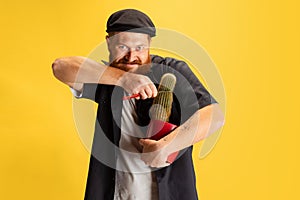 Comic portrait of stylish red-bearded man, barber in black cap having fun isolated over yellow background. Concept of