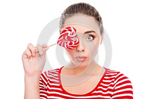 Comic young woman holding a lollipop near her eyes and pouting