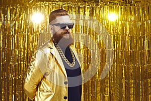 Comically serious cool bearded man in sunglasses stands on a golden background.