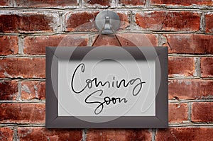 Coming soon. Handwritten inscription in a wooden frame. Brown brick wall