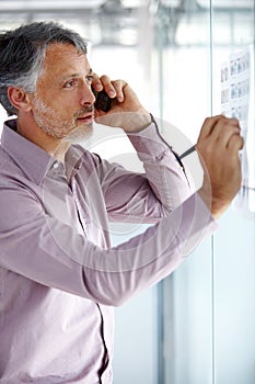 Coming up with the best strategy for his client. A mature businessman talking on his cellphone while writing something