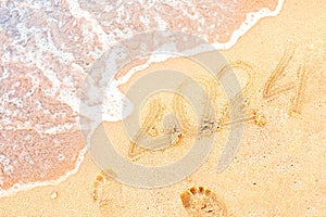 The coming year is 2024. Happy New Year by the sea. Ocean wave washes away sand near the inscription on the sand in the