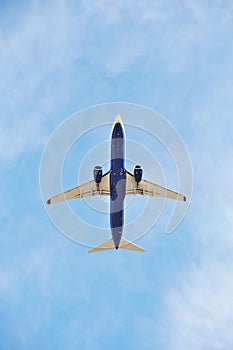 Commercial airplane captured from below as it climbs into the vast blue sky, showcasing its underbelly and jet engines