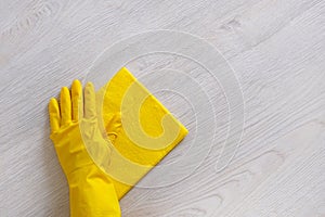 Commercial cleaning company concept. Hand in rubber protective glove with yellow microfiber cloth is wiping wooden floor. Copy