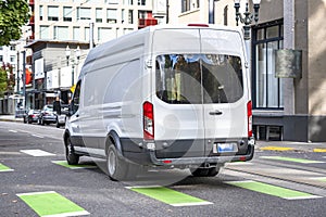 Commercial compact white cargo mini van delivering goods running on the crossroad in the urban city street
