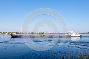 A commercial dry cargo ship sails along the river in summer or early autumn