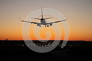 Commercial passenger airplane is landing on the airport runway during sunset