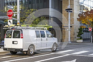 Commercial small business compact mini van with ladders on the roof running on the urban city street crossroad intersection photo