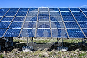 Commercial utility installation of blue photovoltaic panels on a sunny day, foundation pillars below and blue sky above, green pow